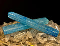 Two 6-inch blue dyed selenite charging sticks resting on a bed of smaller clear quartz crystals.