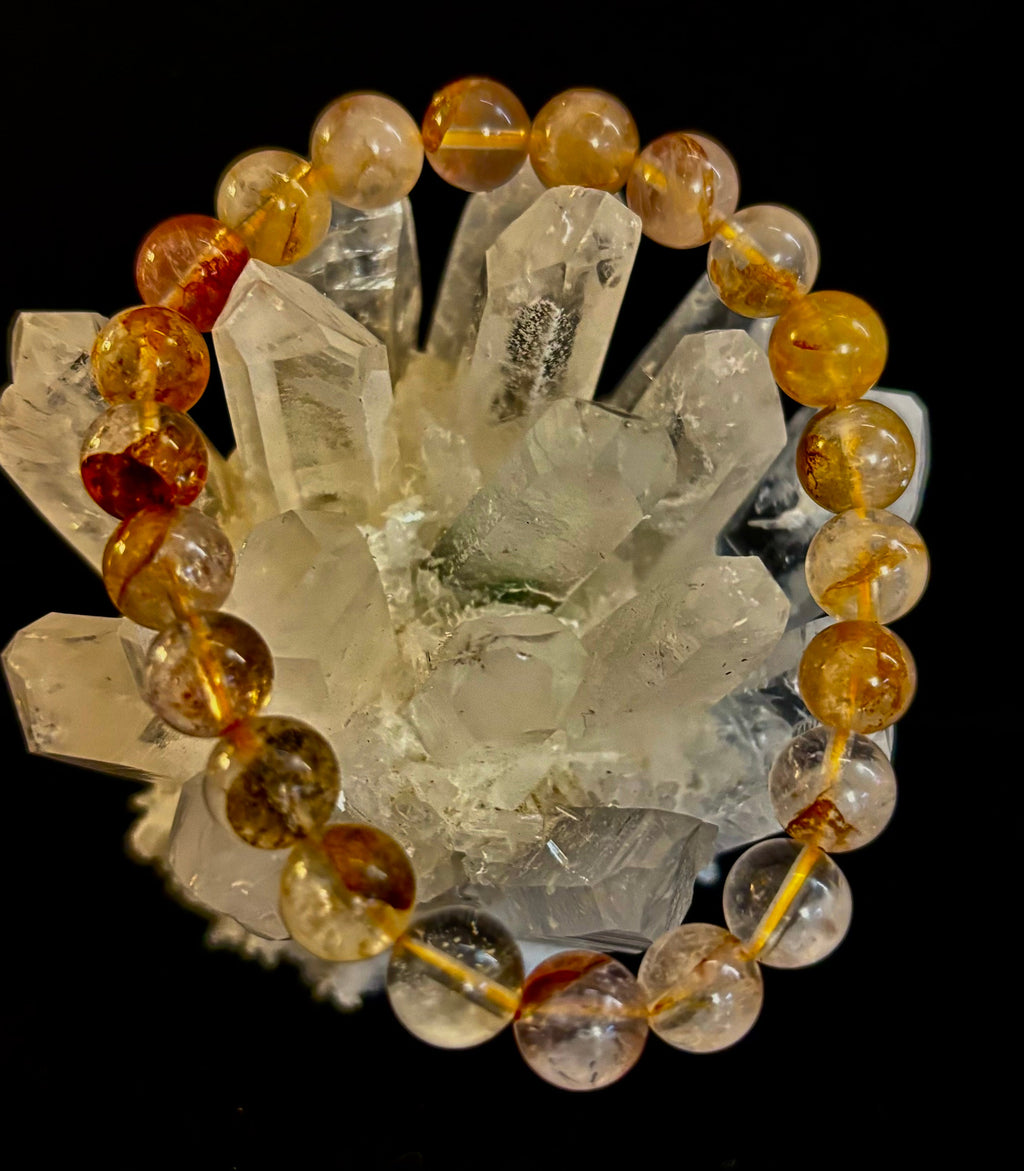 Close up of a round 8mm Golden Healer Quartz bead bracelet resting on a clear quartz point crystal.