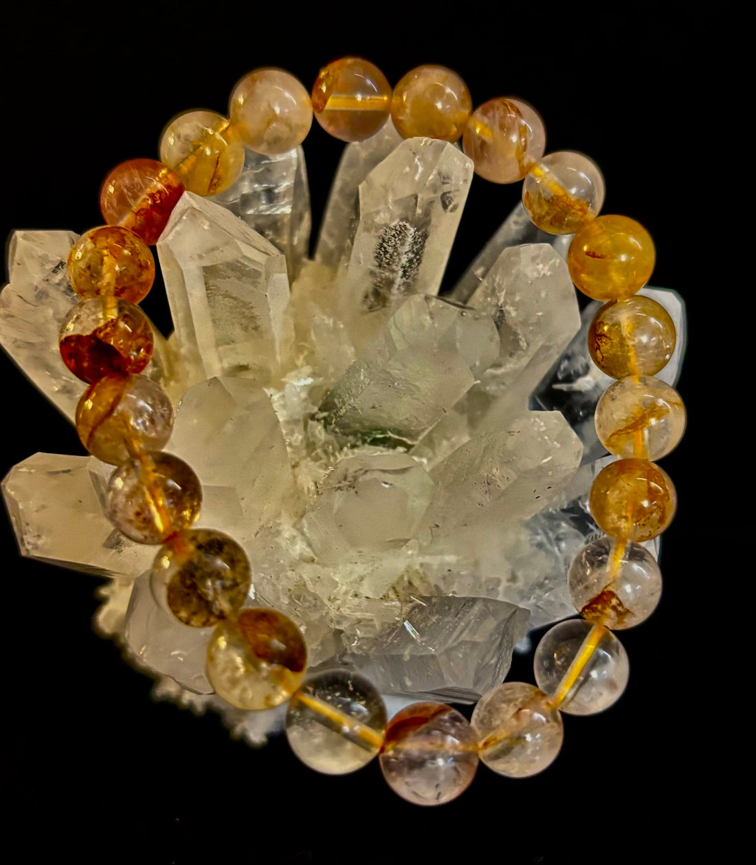 Close up of a round 8mm Golden Healer Quartz bead bracelet resting on a clear quartz point crystal.