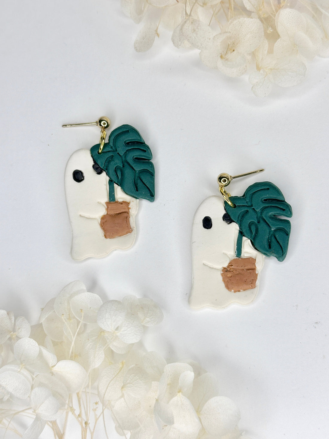 Whimsical Ghost Stealing Monstera earrings featuring white and green leaves with gold detailing.