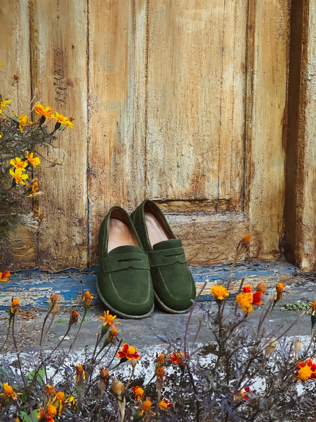 Women's green suede penny loafers featuring a wide toe box and flexible sole standing on stone ground.