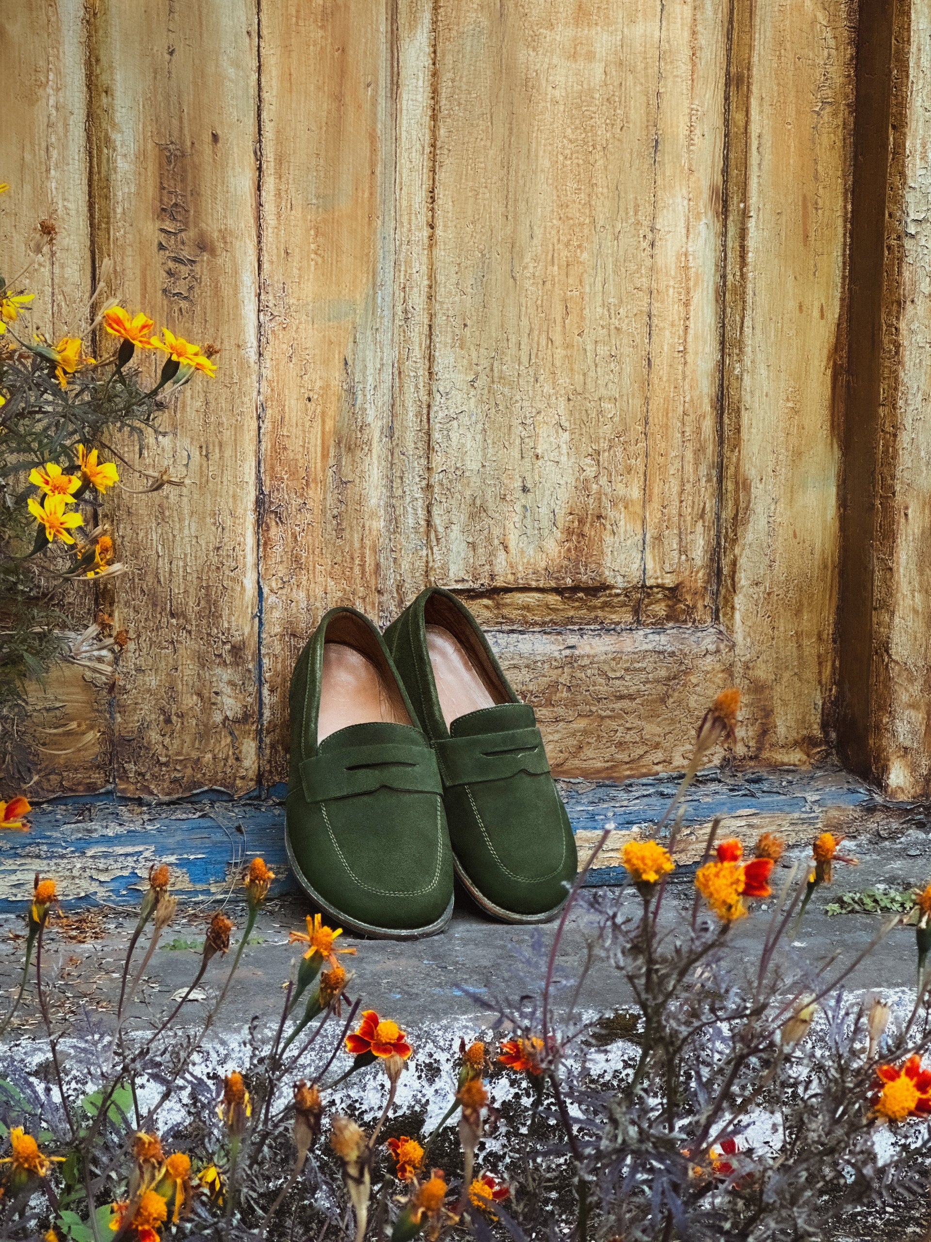 Women's green suede penny loafers featuring a wide toe box and flexible sole standing on stone ground.