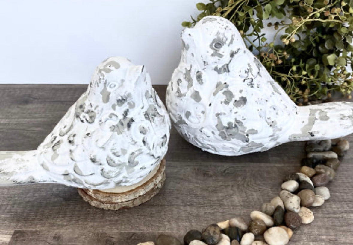 Set of two whitewashed ceramic bird figurines with distressed scroll detailing on a rustic wood surface.