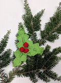 Handmade red and green knit holly ornament hanging on a festive Christmas tree