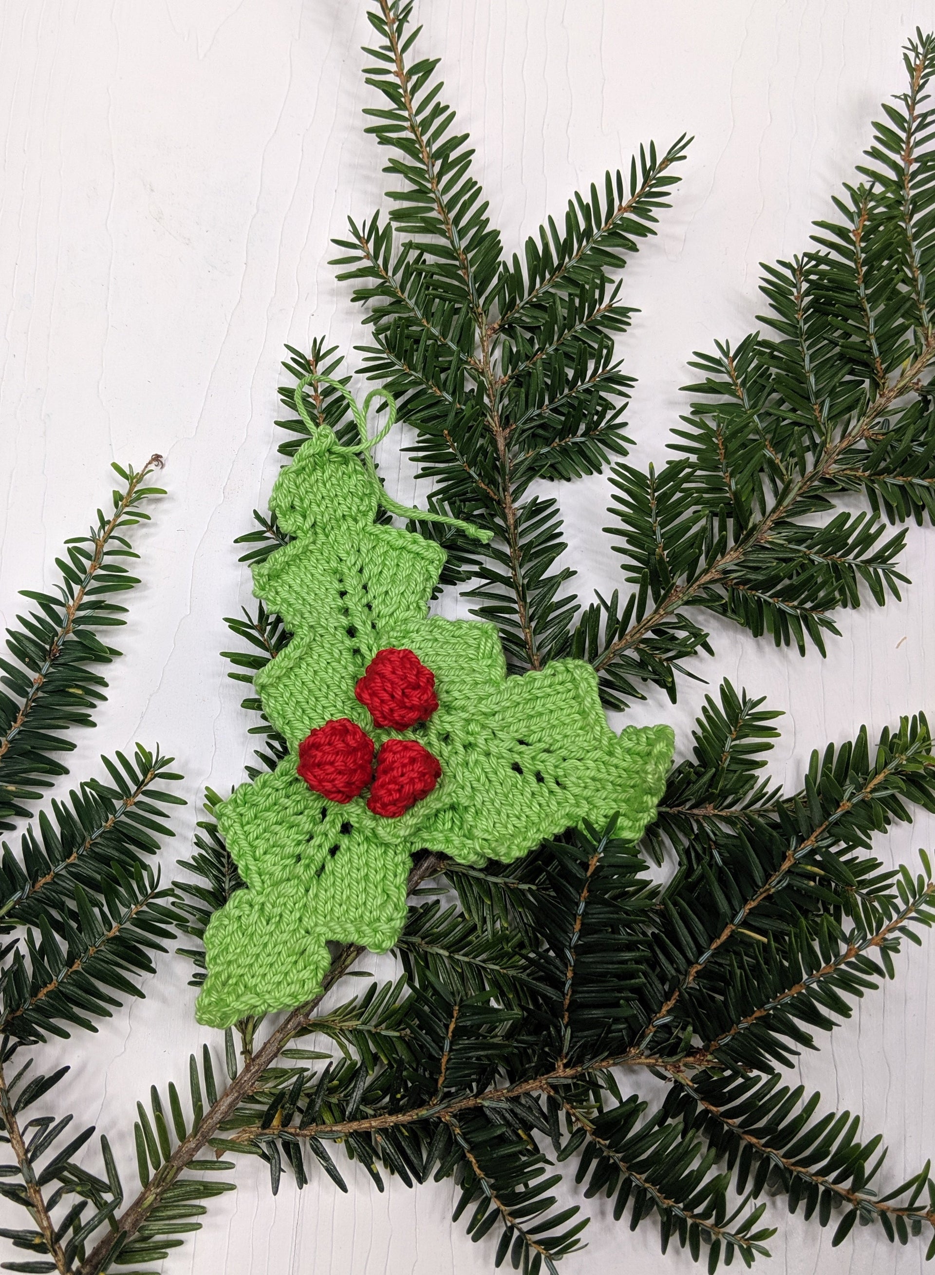 Handmade red and green knit holly ornament hanging on a festive Christmas tree