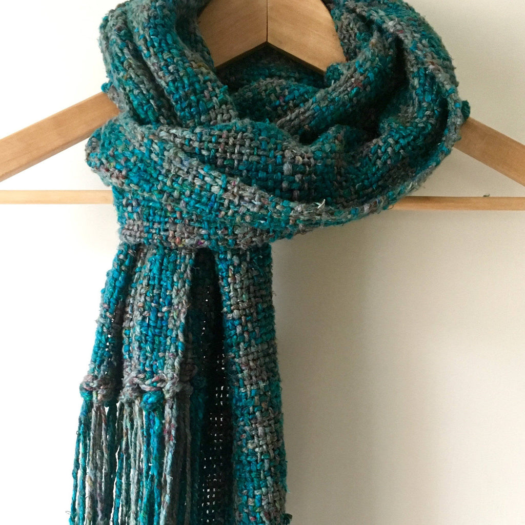 A finished teal and grey checkered woven scarf with fringe details.