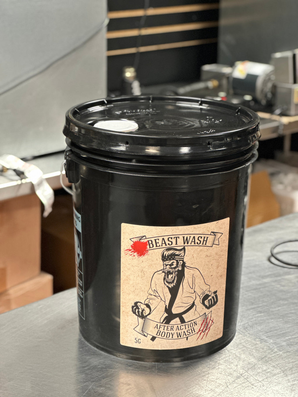 5 Gallon black pail of After Action Beast Wash organic body soap on a metal table.