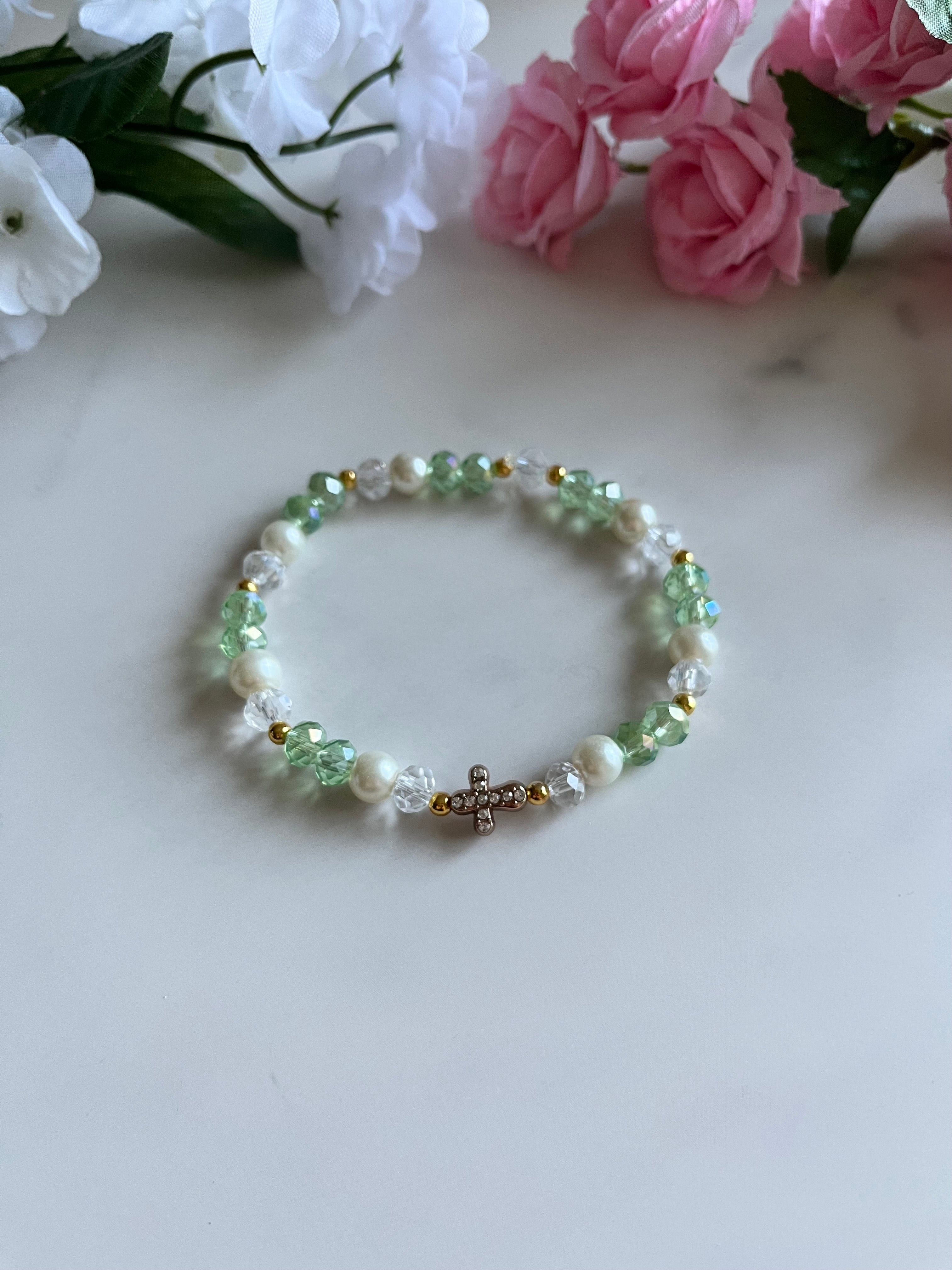 A close-up of a elegant pearl bead bracelet featuring a gold cross charm, styled as religious fashion jewelry.