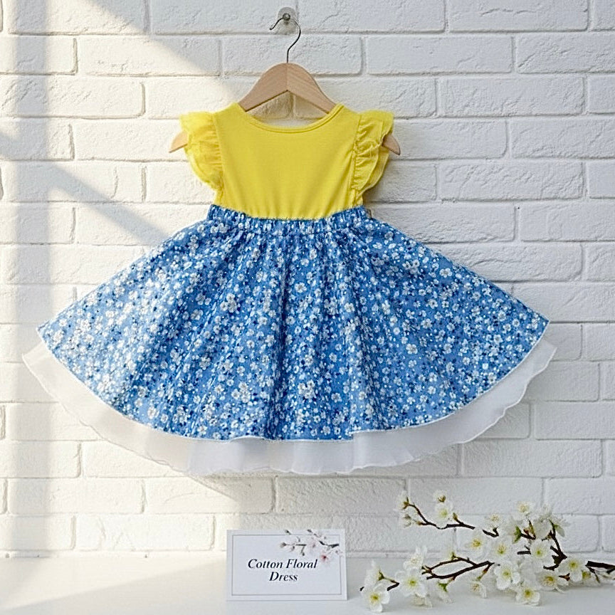 A toddler dress featuring a bright yellow bodice with ruffle sleeves and a blue floral skirt with a white layered hem.