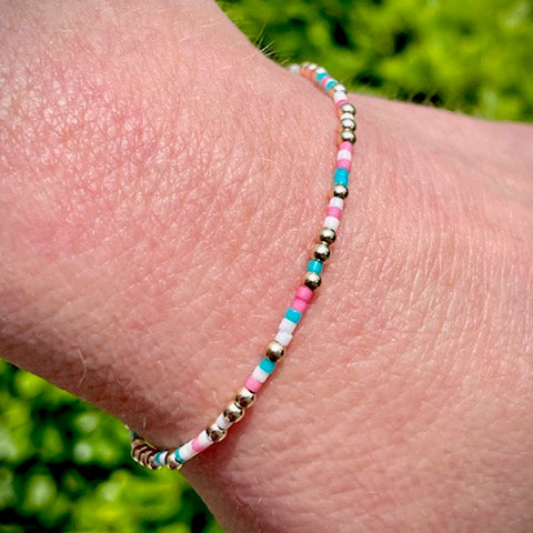 Close up of a wrist wearing a multi-colored bead bracelet with turquoise, pink, and white beads alongside 14K gold-filled beads