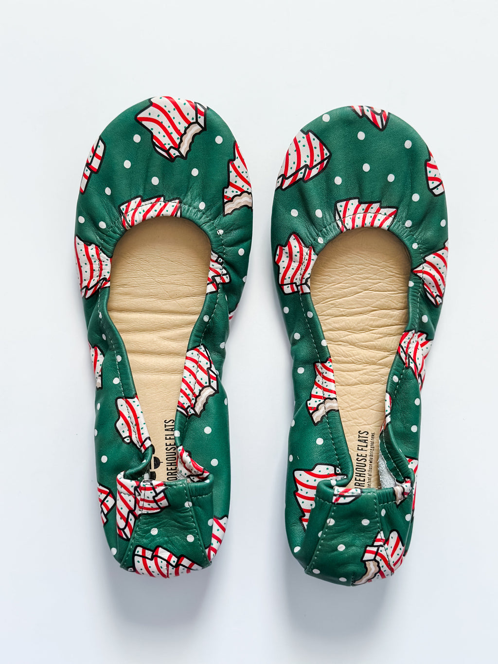 A pair of green holiday-themed ballet flats with a white and red Christmas tree pattern.