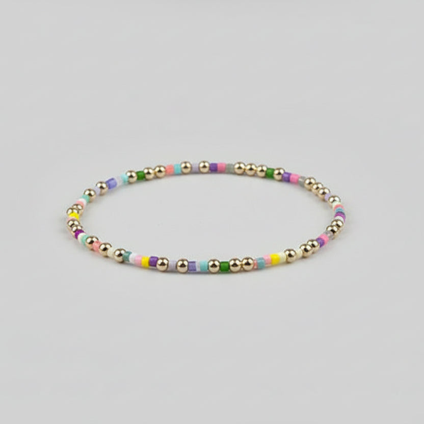 Close up view of a dainty handmade bracelet featuring alternating 14K gold-filled beads and colorful small seed beads on a neutral background.