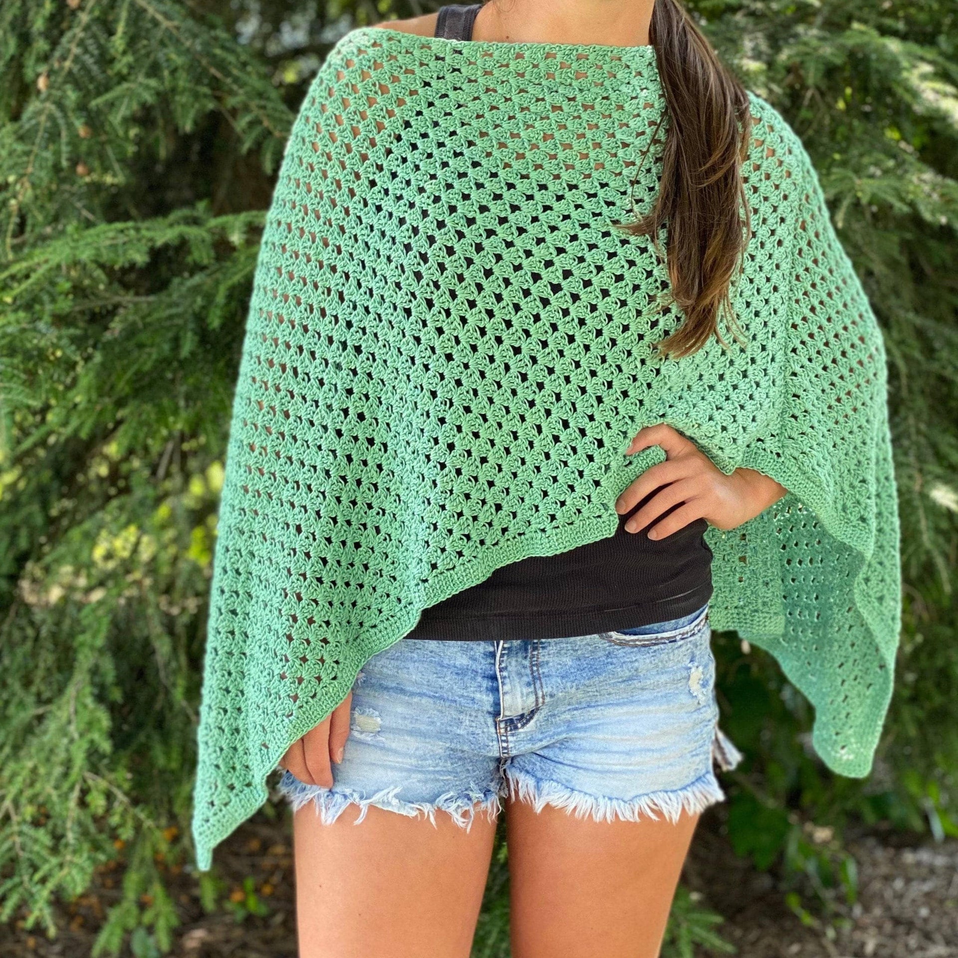 Woman wearing a bright sage green crochet oversized poncho in a bohemian casual style