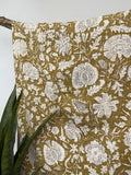 Yellow cotton kantha quilt featuring detailed white floral block print patterns draped over a wooden stand.