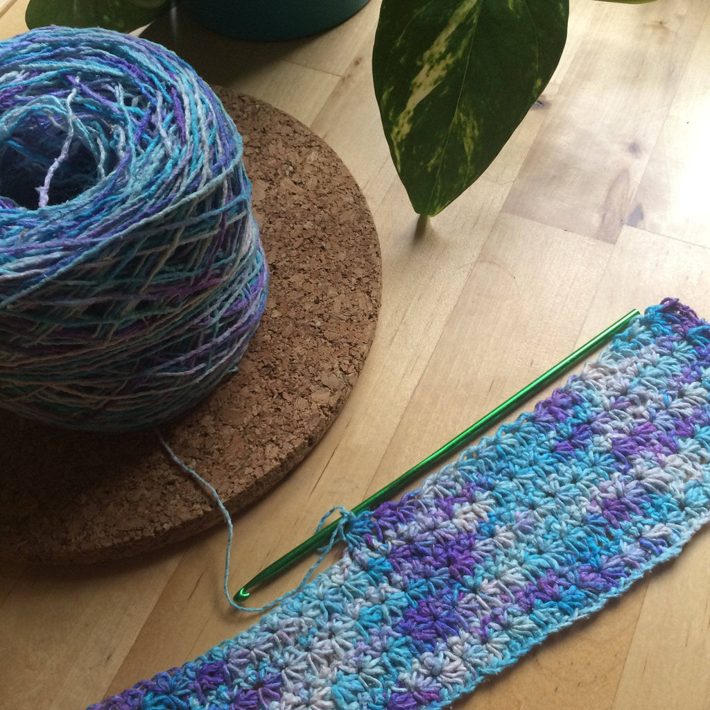 A flat lay of the Floral Garden Placemat Knit & Crochet Kit featuring silk yarn skeins and pattern instructions.