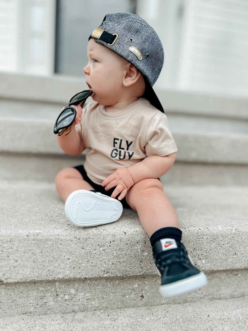 A child wearing a beige minimalist Fly Guy. streetwear t-shirt with bold black text in a lifestyle setting.