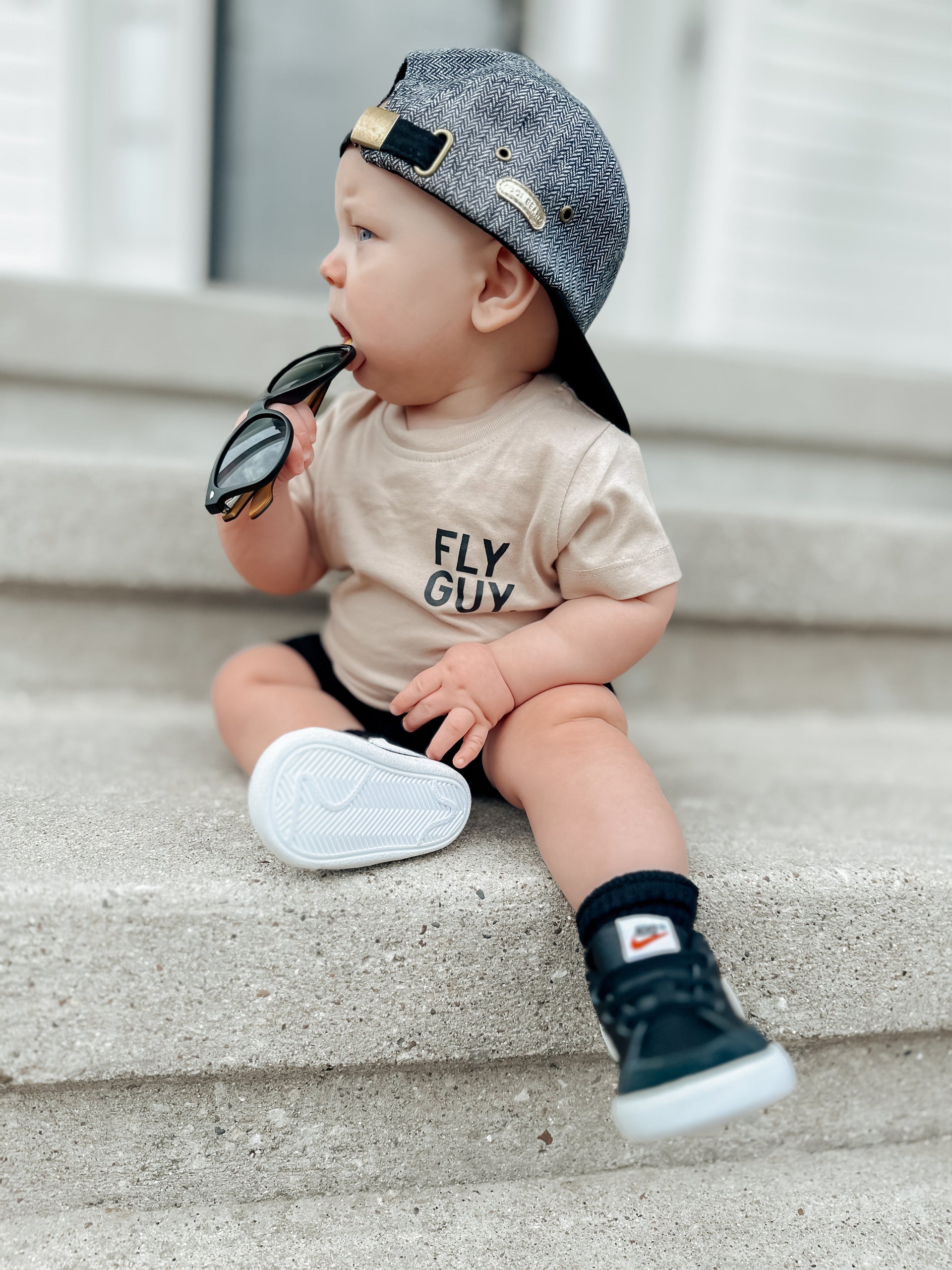 A child wearing a beige minimalist Fly Guy. streetwear t-shirt with bold black text in a lifestyle setting.