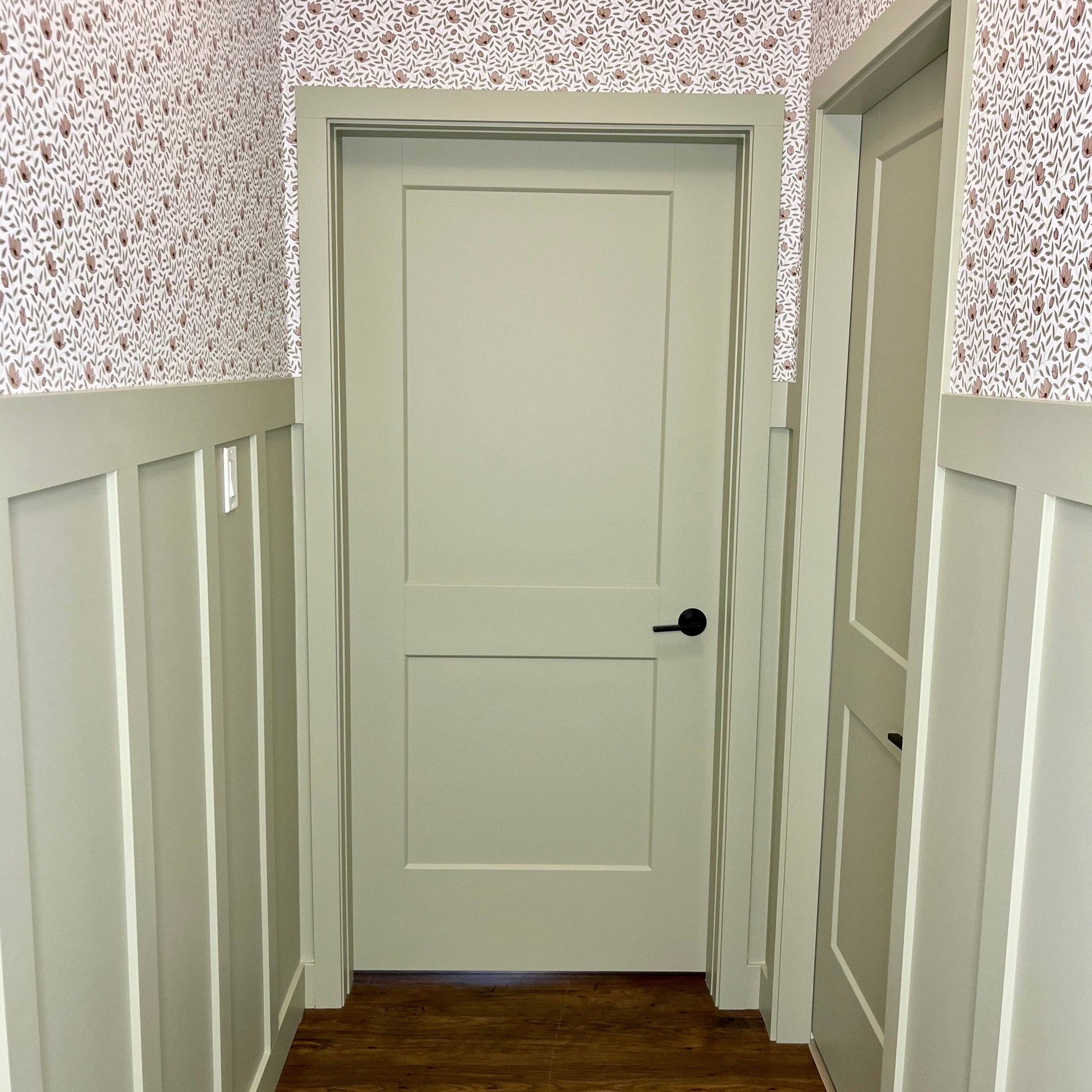 Close up of Eliana floral pattern wallpaper in sage green and off-white on a living room wall