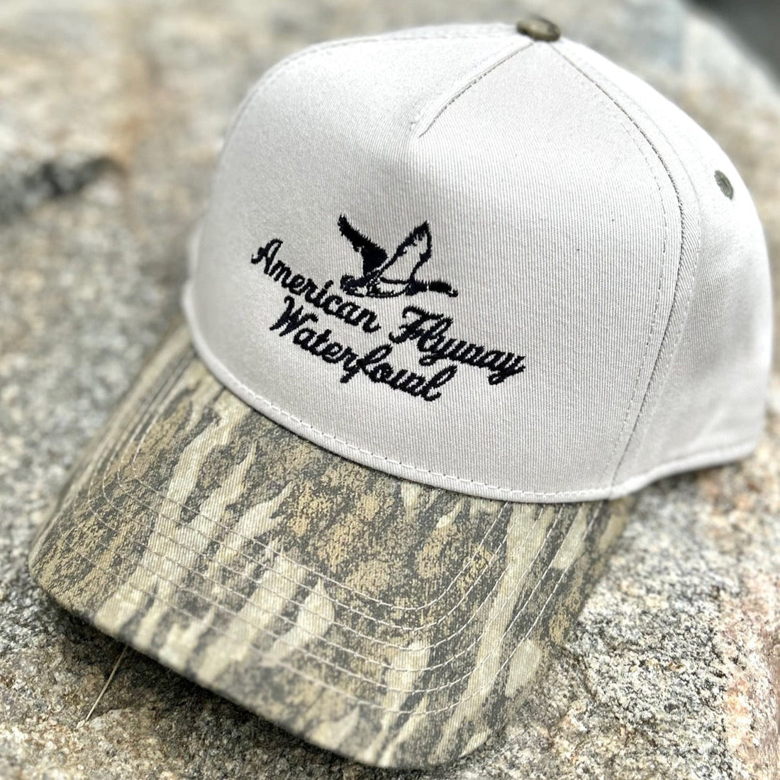 Unisex trucker hat with beige front panels and a Bottomland camouflage brim featuring a snapback closure.