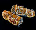 A close up view of a 4-inch white sage smudge stick decorated with dried orange slices and a cinnamon stick, tied with cotton string.