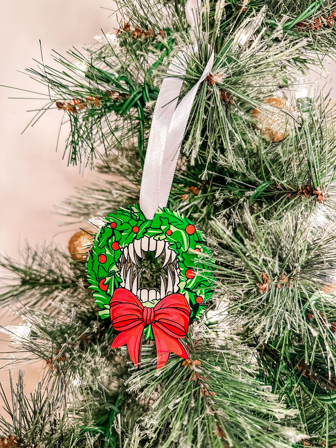 A wooden vampire wreath Christmas ornament with holly and a red bow hanging on a tree.