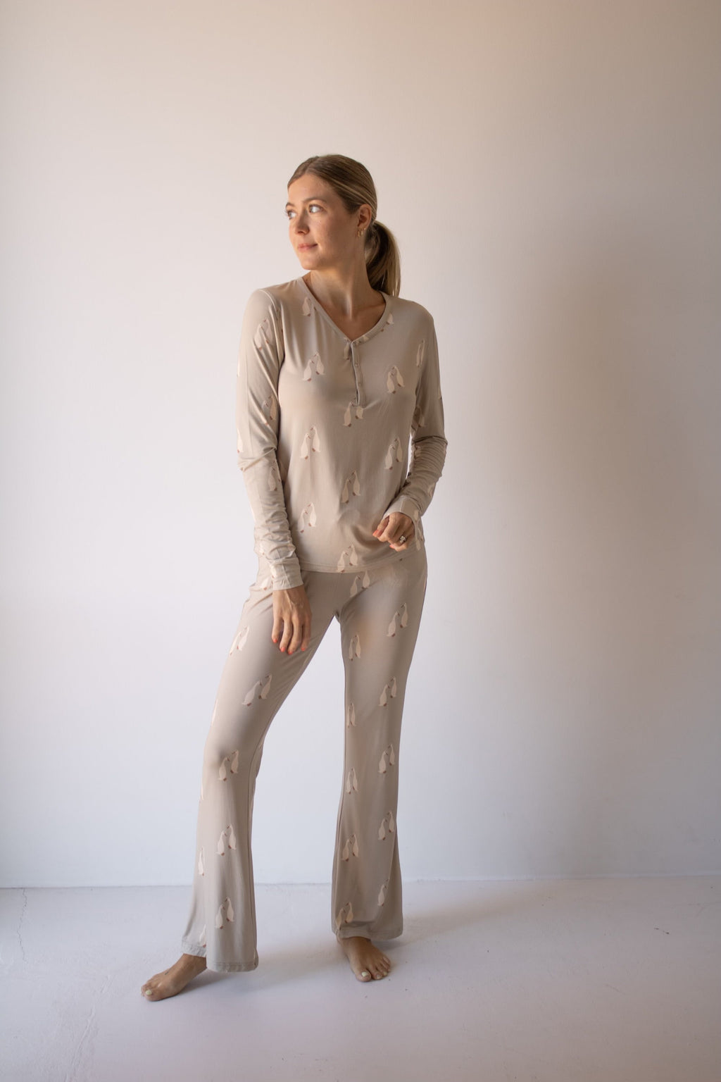 A woman wearing a beige long sleeve pajama top and flared bottoms with a Silly Goose print, standing against a neutral background.