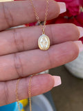 Gold necklace with a pendant held between fingers against a blurred background