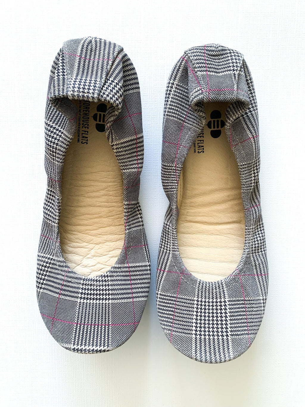 A pair of women's ballet flats with a classic plaid pattern and pink detail accents, shown from top-down and bottom-up views.