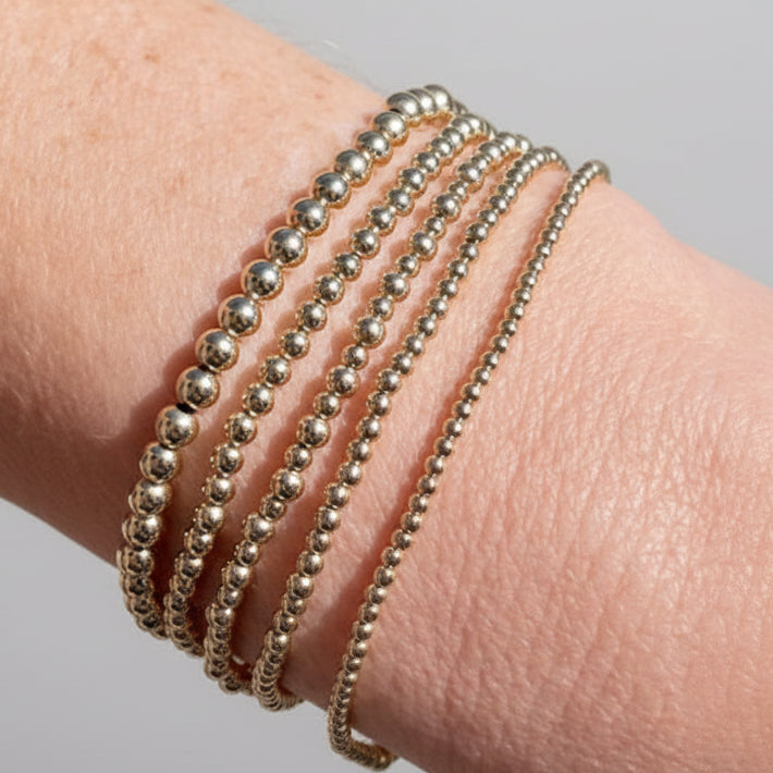 Close up of five 14K gold-filled beaded bracelets of varying sizes stacked on a wrist.