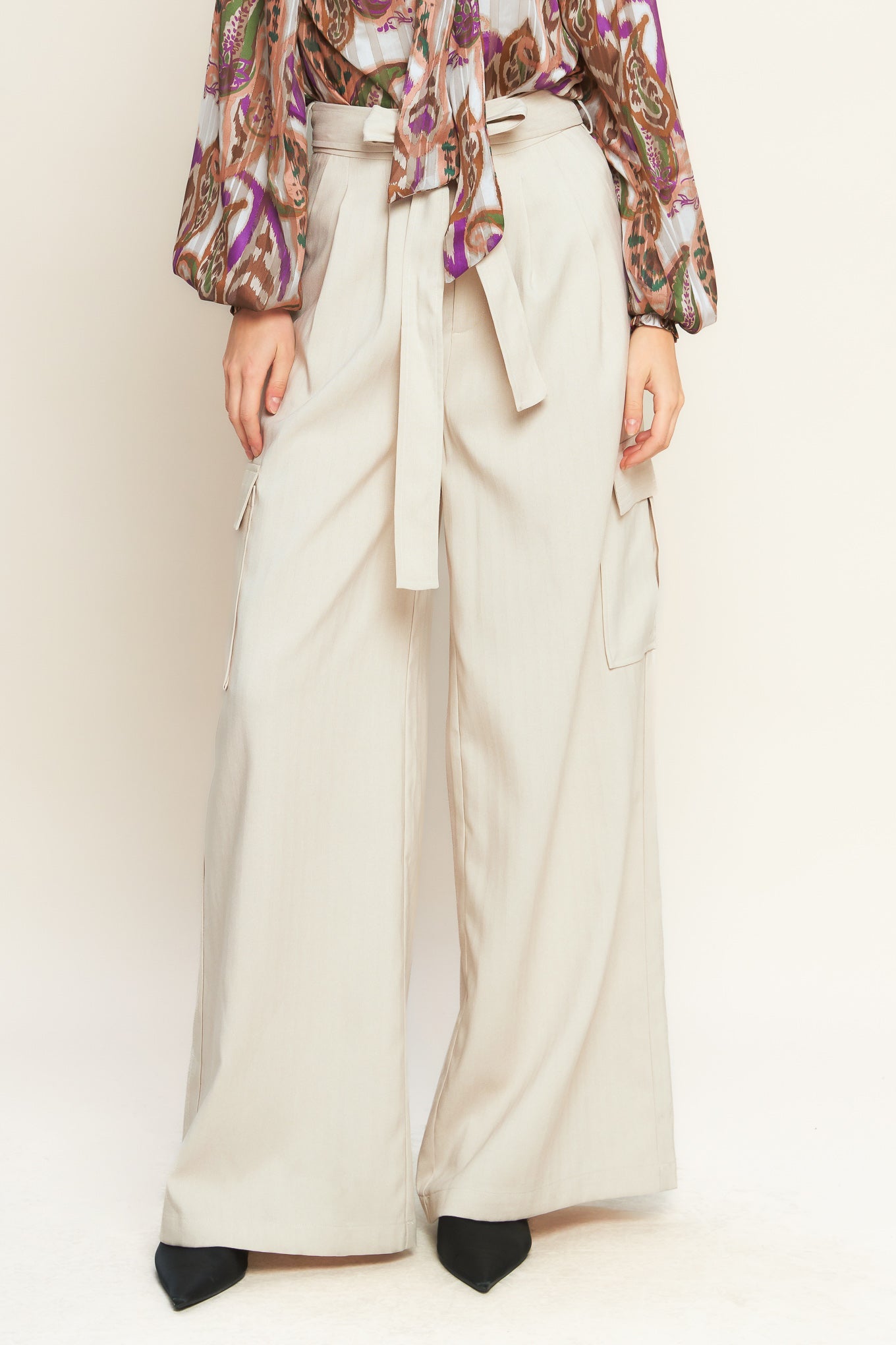 A pair of beige wide leg cargo pants with a tie waist and pleat detail on a model.