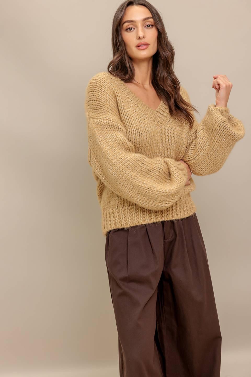 A woman wearing a tan long sleeve chunky V-neck sweater knit top