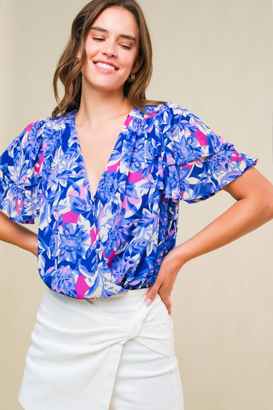 A woman wearing a vibrant blue floral print wrap blouse with flutter sleeves against a neutral background.
