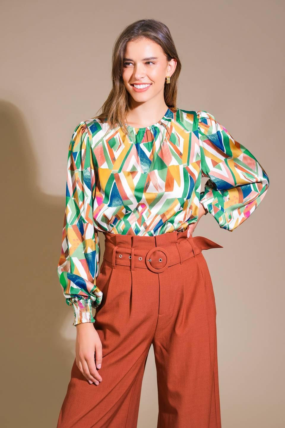 Model wearing a vibrant geometric print long-sleeve blouse with smocked cuffs and a round neckline.