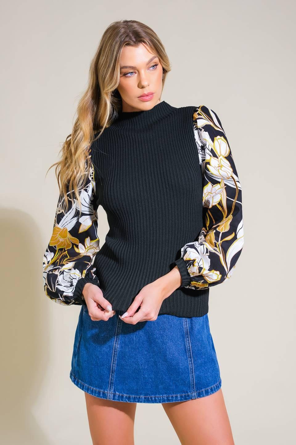 A model wearing a black mock neck sweater top with long floral printed sleeves, styled with a blue denim skirt.