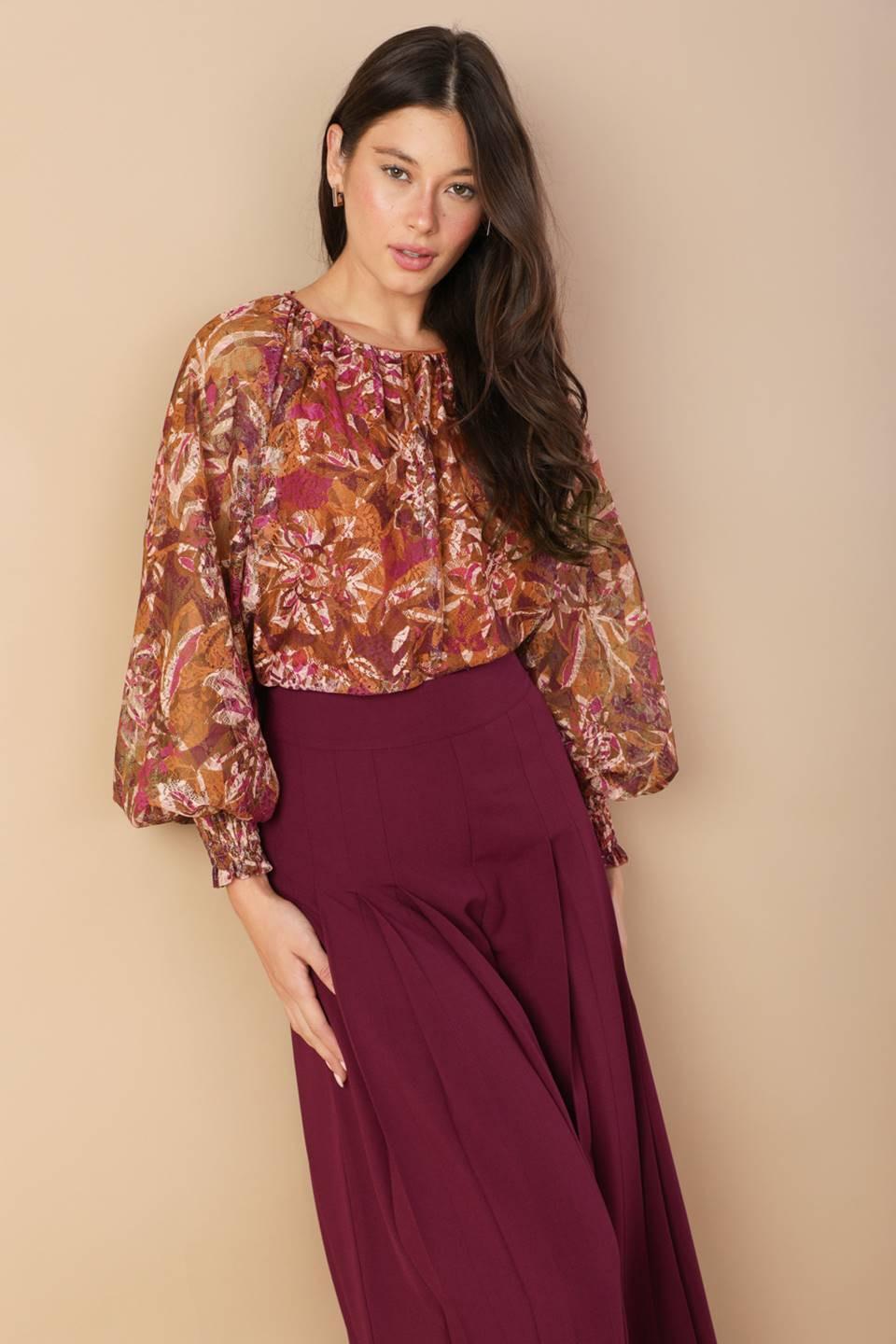 A woman wearing a brown and magenta floral print woven top with long blouson sleeves and smocked cuffs.
