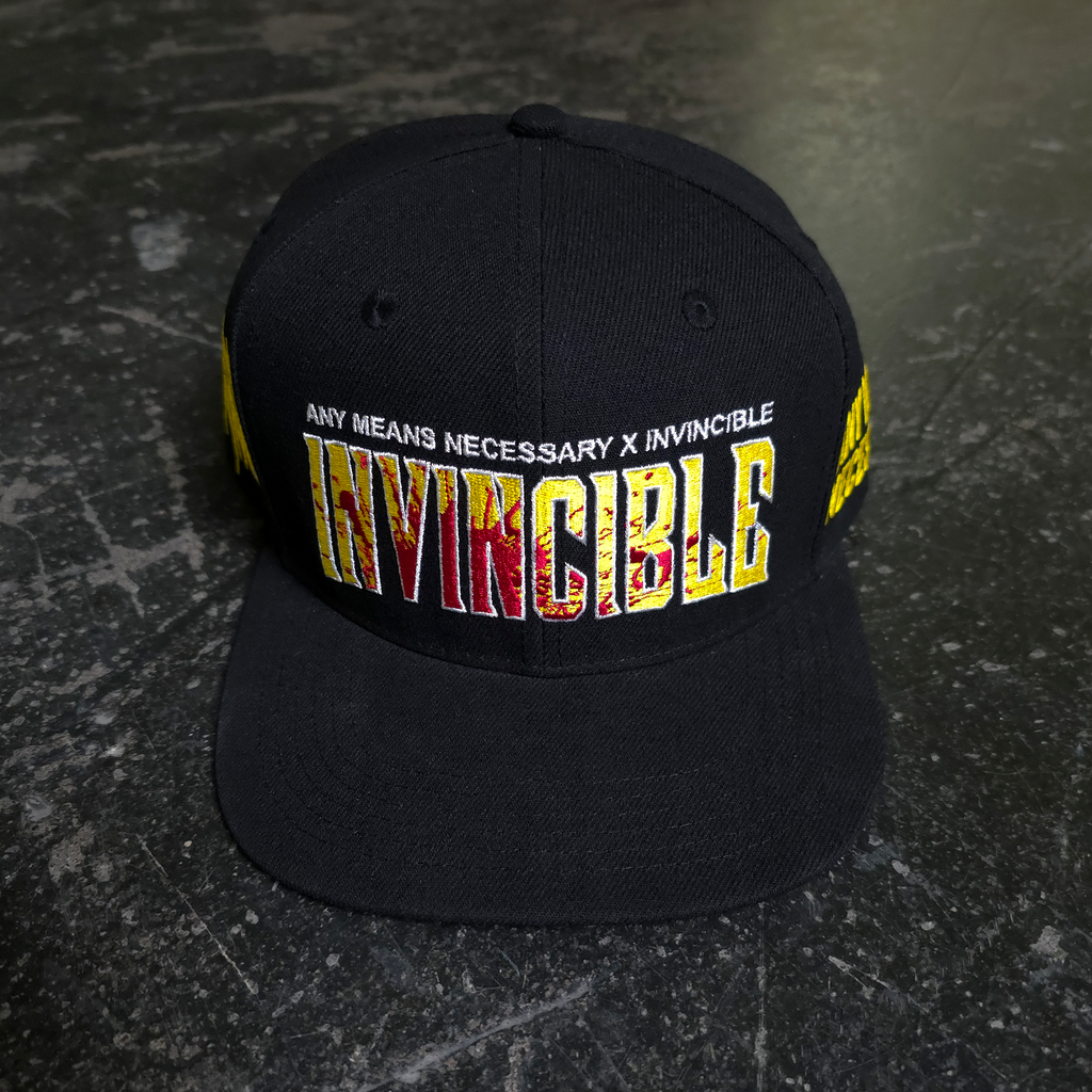 A black snapback cap with yellow and red embroidered text reading INVINCIBLE on the front.