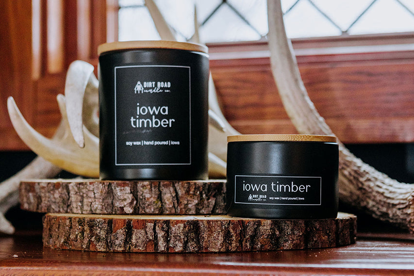Black matte soy candle jar with wooden lid placed on a rustic wood slice surrounded by antlers