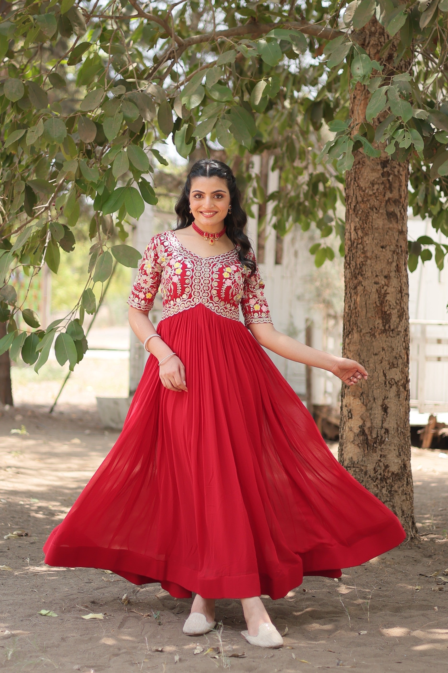 Woman wearing a floor-length red Anarkali dress with gold Zari and sequin embroidery.