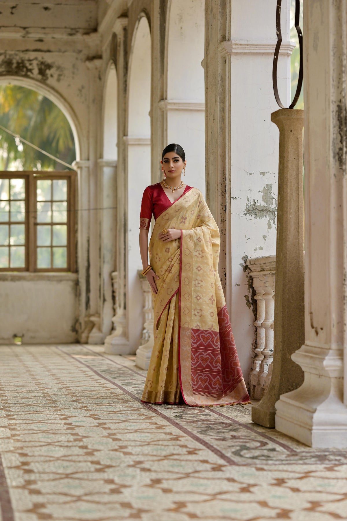 Woman wearing a cream soft raw silk saree with intricate gold zari woven border and matching blouse
