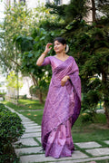 Woman wearing a purple handloom raw silk saree with detailed weaving and matching unstitched blouse.