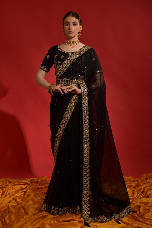 Woman wearing a black georgette saree with sequence coding embroidery and a matching blouse.