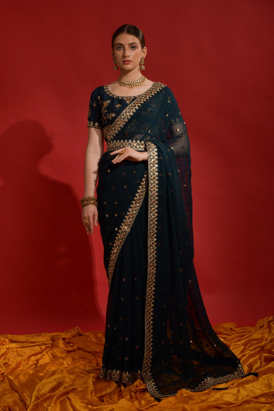Woman wearing a teal chiffon saree with gold sequence coding embroidery and a matching blouse