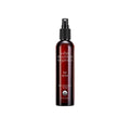 Amber glass bottle of John Masters Organics hair spray with black pump mechanism on a minimalist background