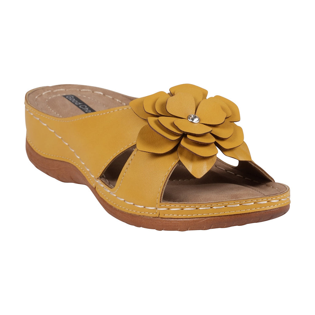 A pair of yellow flat sandals featuring a large decorative fabric flower on the strap, shown from a side angle.