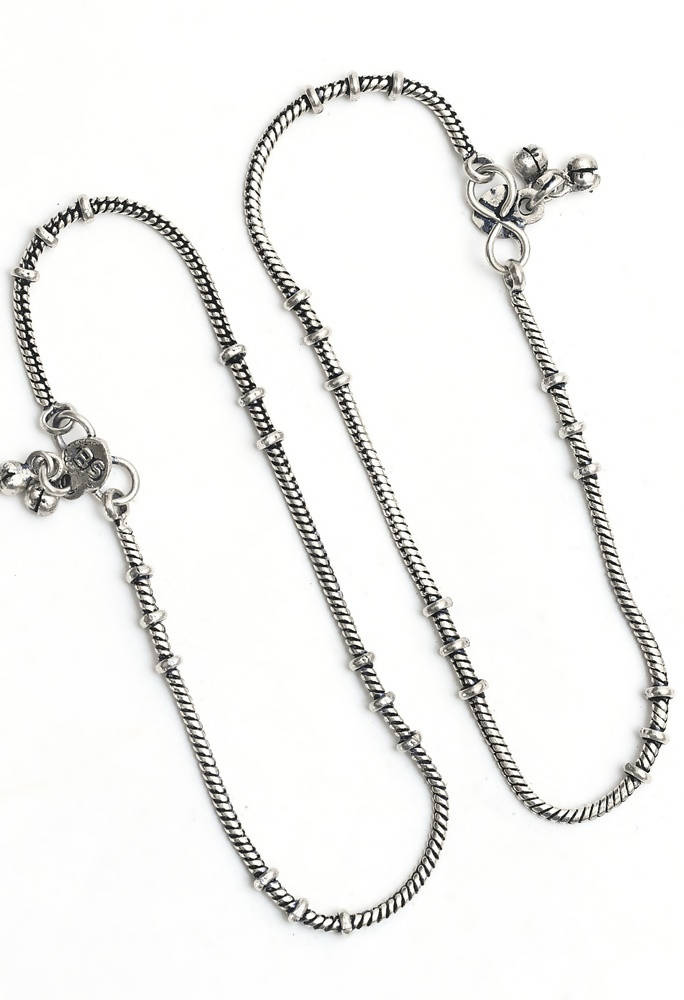 A pair of elegant oxidised silver anklets with traditional Kamal Johar designs on a neutral background.