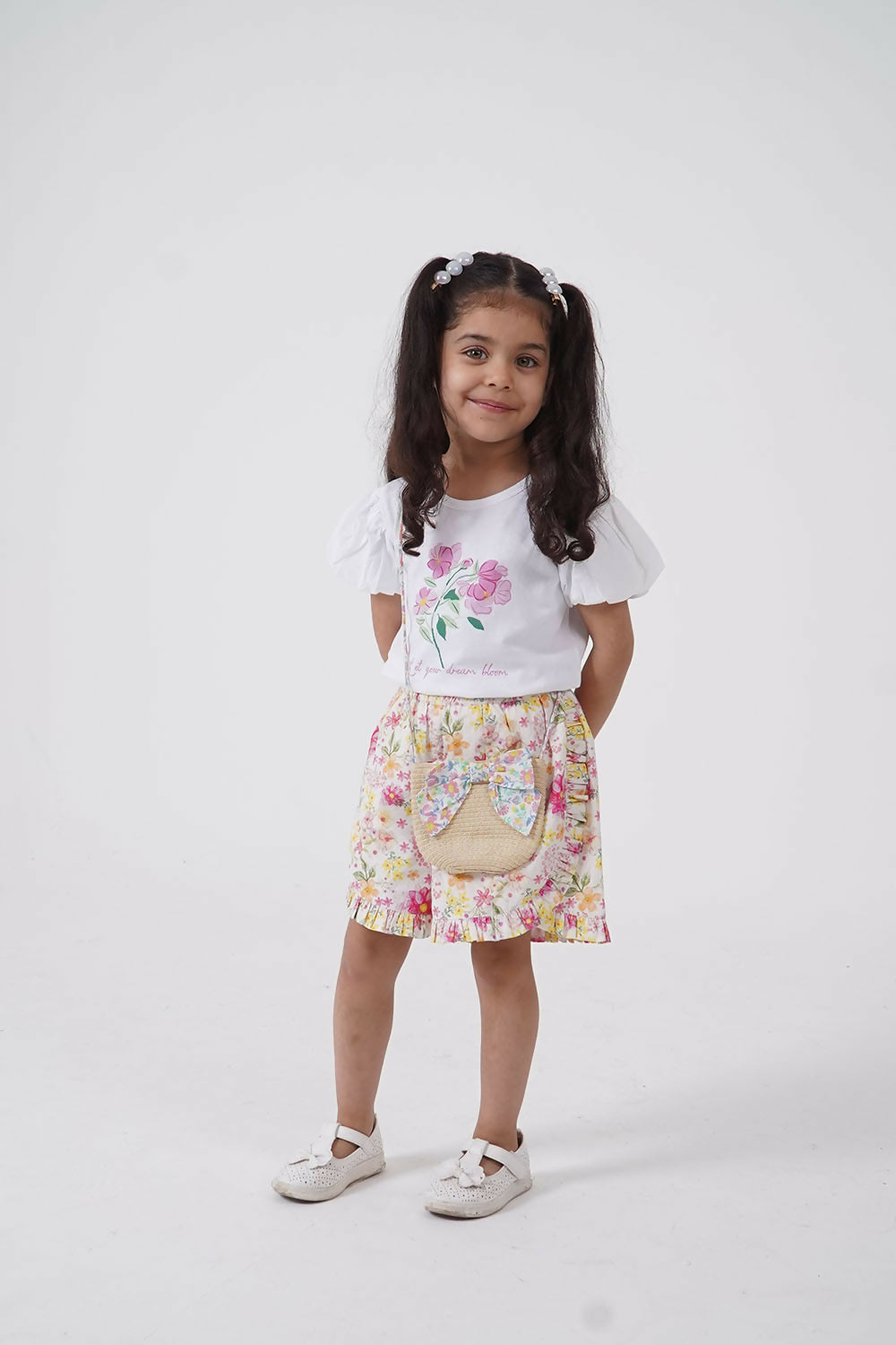 A young girl wearing a floral puff sleeve tee and matching shorts set available in white, pink, and yellow.