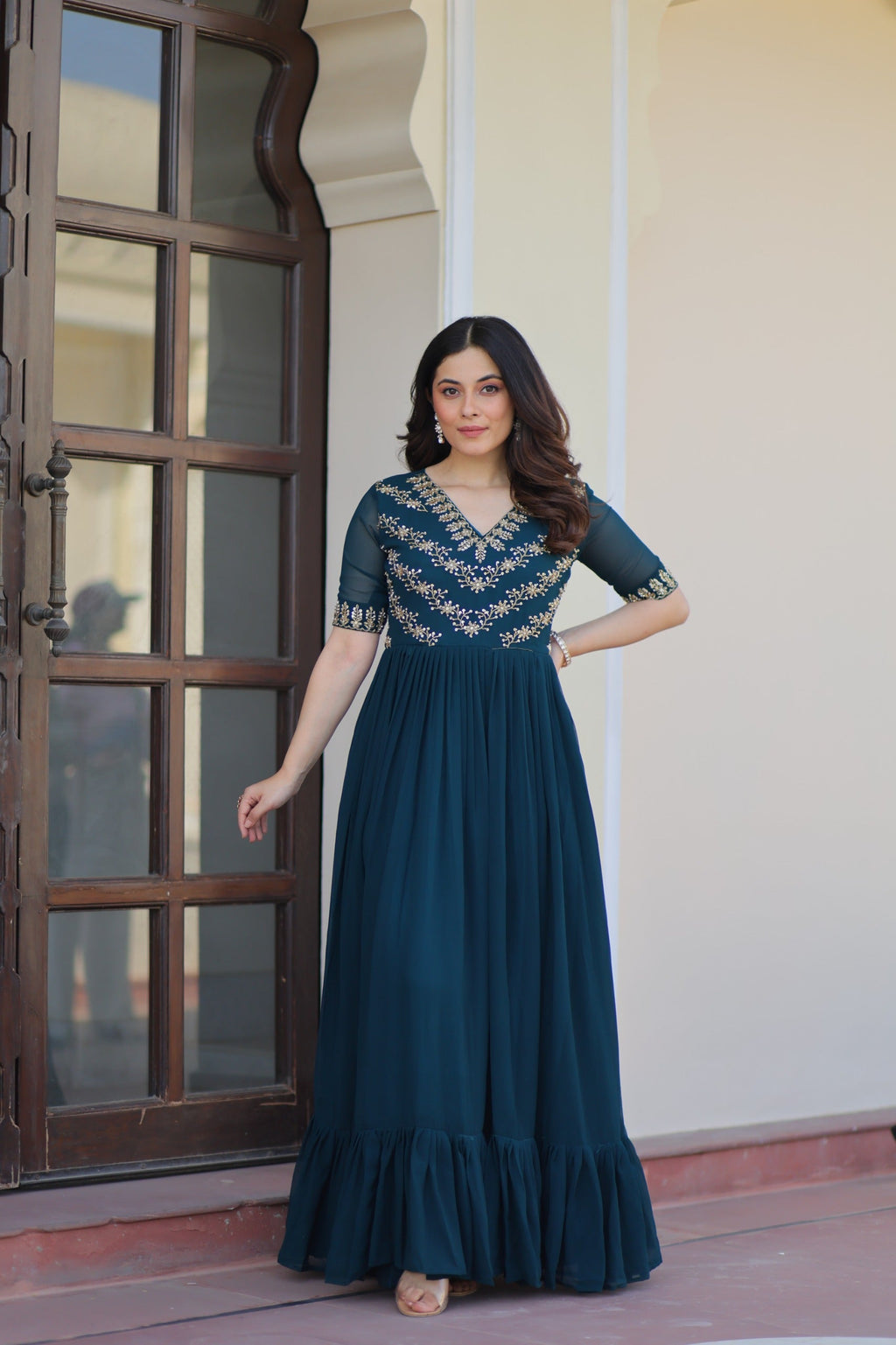 Woman wearing a Rama color georgette gown with intricate multithreaded beadwork and embroidery.