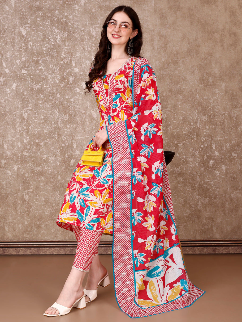 A woman wearing a pink floral printed cotton kurta set with matching pants and dupatta.