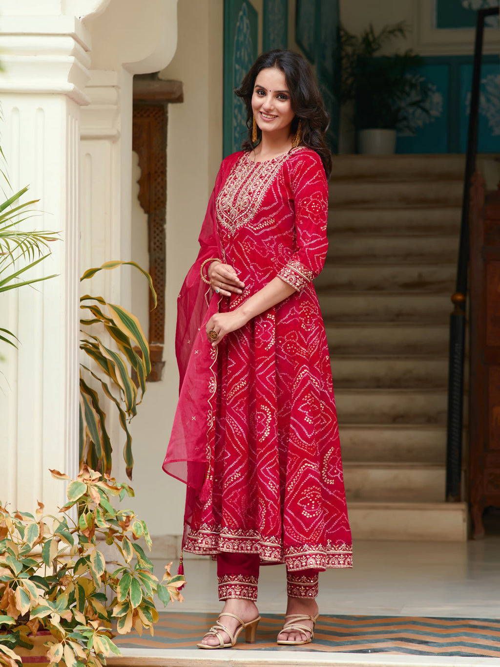 Woman wearing a Rani colored embroidered Bandhani flared kurta set with matching pants and printed dupatta