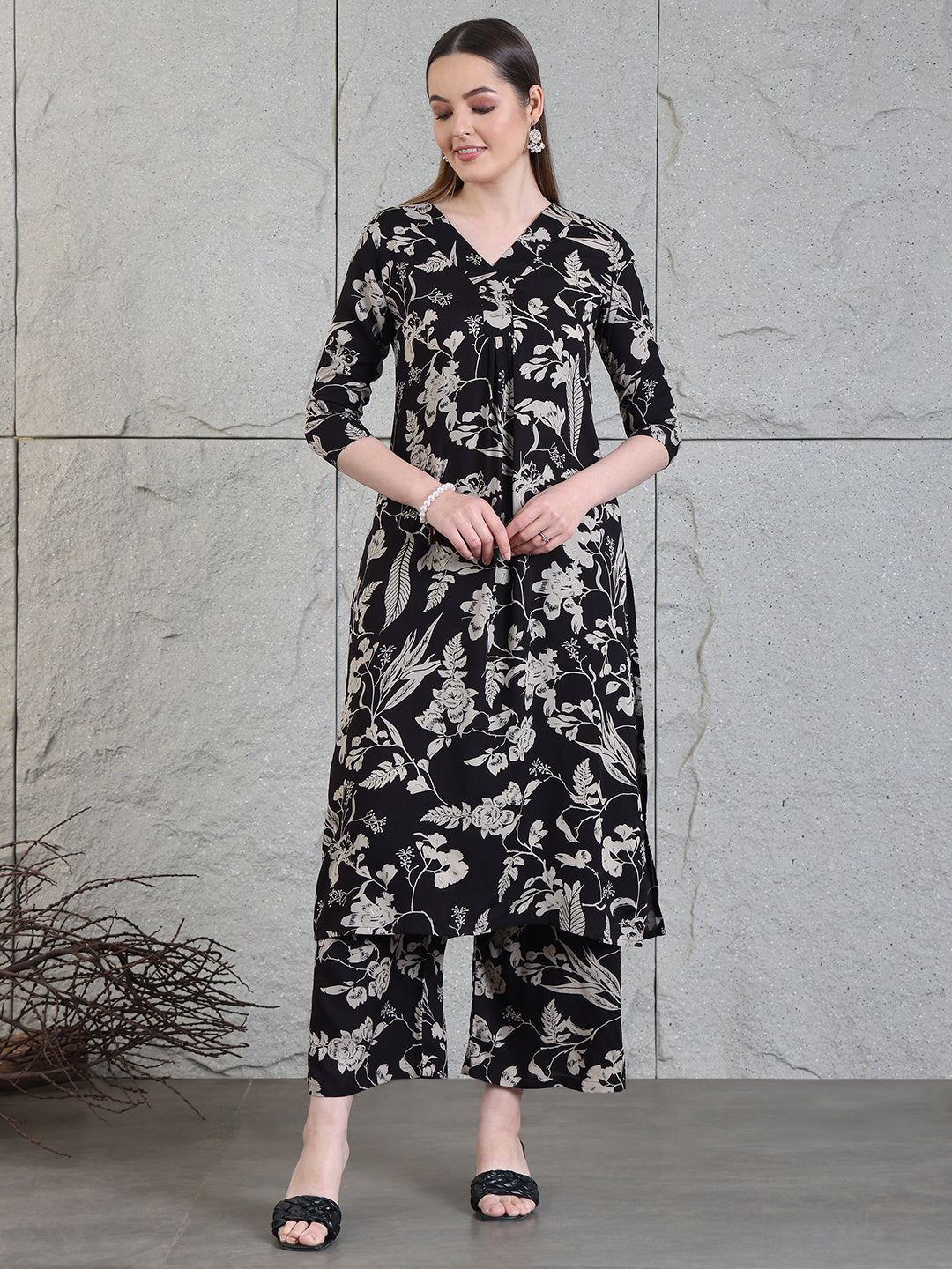 A woman wearing a black botanical printed kurta with matching palazzo pants, featuring a V-neck and 3/4th sleeves.